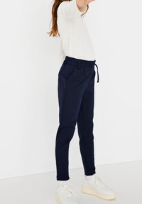 Námořnické modré tapered kalhoty s elastickým pasem a šňůrkou, s bočními kapsami a hladkým, texturovaným materiálem.