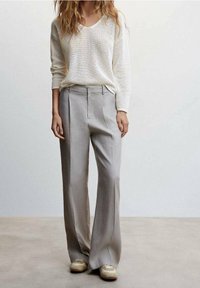 Leichter, creamfarbener Strickpullover mit V-Ausschnitt; kombiniert mit hoch taillierten, weit geschnittenen hellgrauen Hosen; Sneaker mit beigen Akzenten.