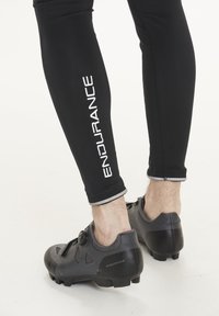 Svarta atletiska leggings med "ENDURANCE" tryckt i vitt, kombinerat med svarta cykelskor med en strukturerad yta och en rattstängning.