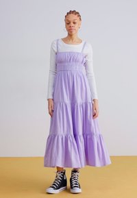 Rochie maxi din lavandă, în straturi, cu talie elastică și bretele subțiri, asortată cu adidași negri cu vârf înalt. Textură de bumbac neted.