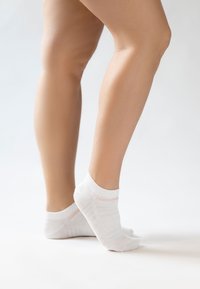 Λευκές βαμβακερές κάλτσες μέχρι τον αστράγαλο με ροζ λωρίδα, που διαθέτουν ριγωτή υφή και άνετη εφαρμογή, τοποθετημένες σε ουδέτερο φόντο.