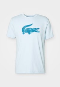 Light blue cotton t-shirt featuring a teal crocodile graphic on the front, with a round neck and short sleeves. Smooth texture.