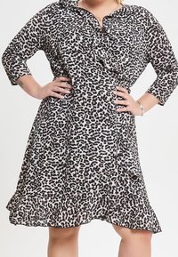 Klänning med leopardmönster, krage, 3/4-långa ärmar, knappstängning, volangkant, tillverkad av lätt tyg i svart och beige nyanser.