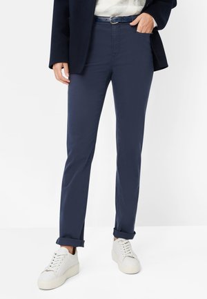 Pantaloni chinos blu navy a taglio slim, con tasche frontali, orlo arrotolato e cintura blu coordinata, abbinati a sneakers bianche.