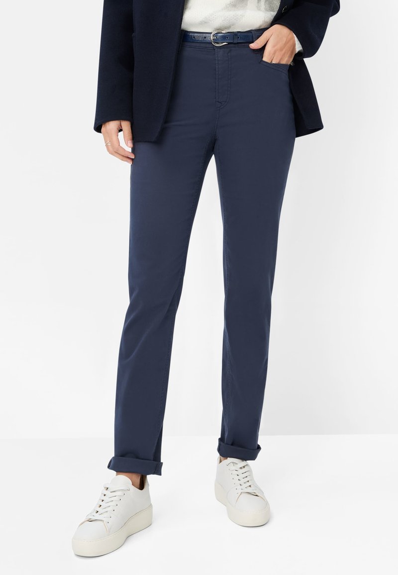 Marineblå chinos med slim fit, der har forlommer, opsmøgede kanter og et matchende blåt bælte, stylet med hvide sneakers.