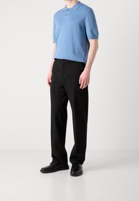 Polo bleu clair à manches courtes avec patte de boutonnage, porté avec un pantalon noir et des chaussures noires. Texture lisse, coupe régulière.