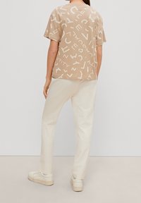 Beige t-shirt med hvide abstrakte bogstaver, kortærmet og afslappet pasform, parret med lysecreme bukser og hvide sneakers.