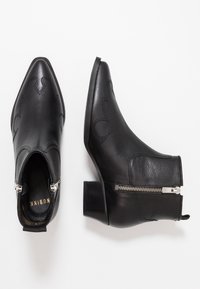Botas de cuero negras hasta el tobillo con puntera puntiaguda, que cuentan con costuras decorativas y una cremallera en el lateral. Tacón grueso y textura suave.