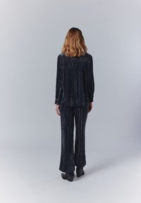 Tengerészkék velúrból készült kétszdás ruházat, amely hosszú ujjú felsőből és bő szárú nadrágból áll, texturált, függőleges csíkozással.