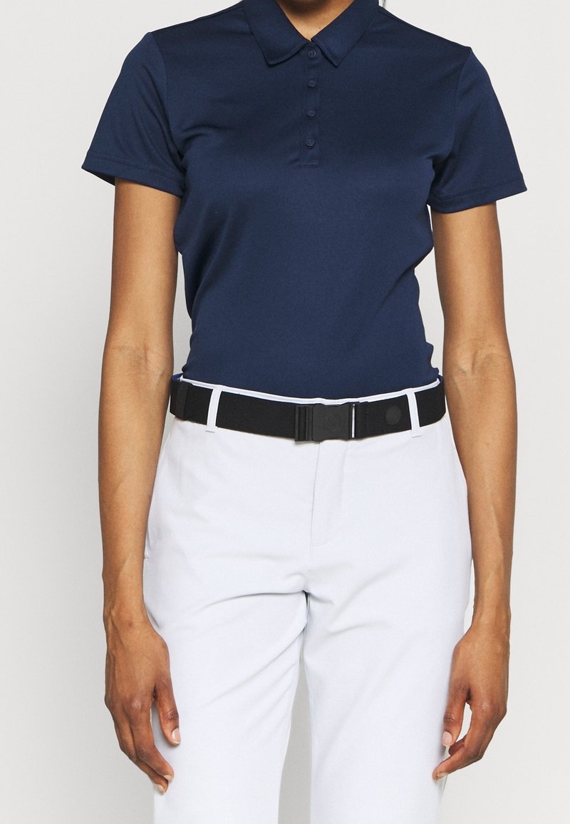 Navy polo shirt with a collar, featuring a button placket and short sleeves. Paired with light gray pants and a black belt with accents.