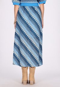 Maximekra dress, jossa on sininen kuvio, jossa on pyörivää kuviointia eri sävyissä. Hihoissa on puffit, ja mallilla on beiget nilkkurit.