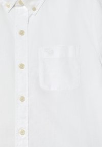 White button-up shirt made of cotton with a collar, featuring beige buttons and a chest pocket with an embroidered deer design.