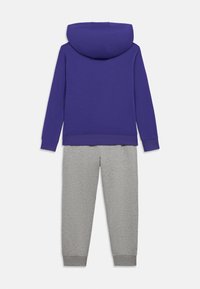 Lilla hættetrøje med frontlomme, parret med grå sweatpants med elastiske manchetter. Casual stof, afslappet pasform.