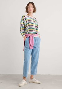 Zebra sweter w kolorach zielonym, różowym, żółtym i fioletowym, z kremowym dekoltem. Jasnoniebieskie dżinsy i różowy sweter związany w talii.
