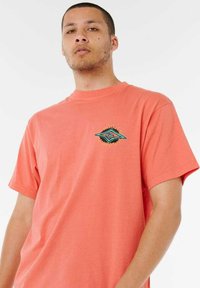 T-shirt in cotone corallo con maniche corte. Presenta un design grafico turchese e nero sul petto. Stile semplice con collo rotondo.