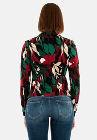 Langarmige top met een patroon van een meerkleurig bladdesign in rood, groen en beige, gemaakt van rekbaar materiaal, met een getailleerde pasvorm.