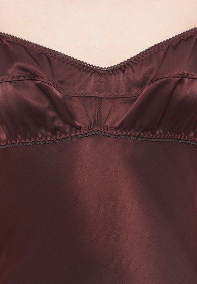 Detailný záber na osobu nosiacu hodvábnu tmavomodrofialovú košieľku so zubatým lemovaním pozdĺž výstrihu a švov.