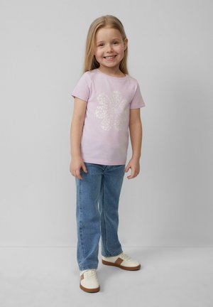 Hellrosa Baumwoll-T-Shirt mit floralem Design, kombiniert mit blauen Jeans und weißen Sneakers mit braunen Akzenten.