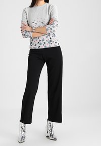 Grå blommönstrad långärmad topp med rosa och blå accenter, i kombination med svarta vida byxor och blanka silvriga ankelstövlar.