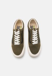 Zapatillas bajas de ante verde oliva con cordones blancos y acentos laterales negros. Presentan una superficie texturizada y una suela de goma.