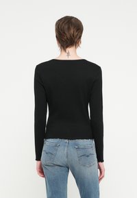 Zwarte lange mouwen top in een geribbelde structuur, met een ronde halslijn en een scalloped zoom, gecombineerd met lichtblauwe denim jeans.