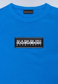 Mėlynas medvilninis marškinėliai su juodu stačiakampiu logotipu ir balta užrašu "NAPAPIJRI geographic", esantis center krūtinėje. Standartinis apvalus iškirpimas.