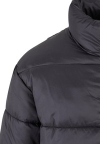 Puffy svart jakke med høy krage, glatt tekstur og horisontal søm. Materialet ser blankt og isolert ut.