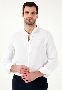 Camisa blanca de manga larga con cuello mao. Hecha de un tejido texturizado, presenta un ligero patrón arrugado y cierre de botones en el frente.