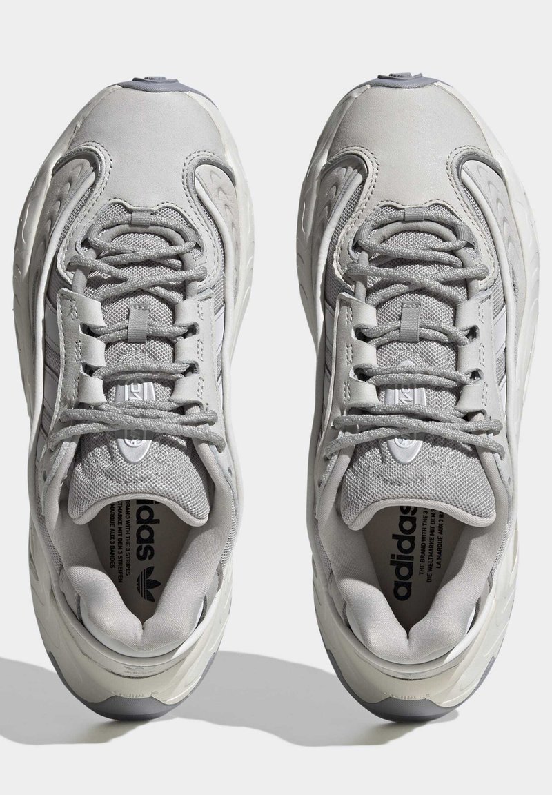 Graue Sportschuhe mit einem strukturierten Mesh-Obermaterial, gepolsterter Zunge und Schnürsenkeln. Sie haben eine abgerundete Zehenpartie und eine dicke Gummisohle.