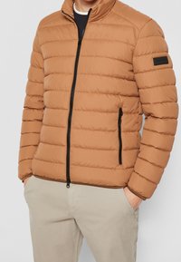 Giacca a vento marrone con motivo a quadri orizzontali, colletto stand, zip frontale e due tasche laterali con zip nera.