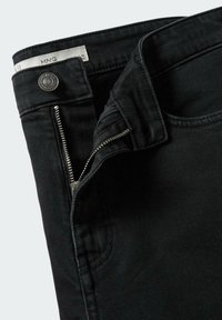 Jeans de mezclilla negra con cierre de cremallera, botón de metal y detalles de costura sutiles. La tela tiene una textura suave y un ajuste clásico.
