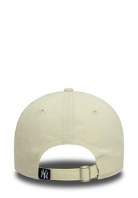 Light yellow baseball cap with a curved brim, adjustable strap at the back, and a black NY logo on the strap. Made of cotton fabric.