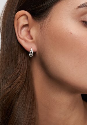 Kvindeøre med langt brunt hår iført en lille sølv ørering med indlejrede klare sten.