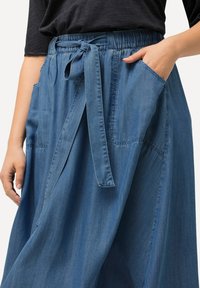 Jeanskjol med en bred, flödande design, elastisk midjeband, knytdetalj och sidofickor, i en medelblå nyans med en mjuk textur.