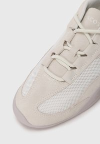 Lys beige sneaker med en kombination af suede og mesh materialer, teksturerede detaljer og cremede snørebånd. Rund tå og gummisål.