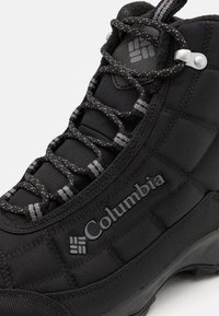 Black waterproof boot featuring a textured fabric upper with quilted design, grey laces, and a prominent Columbia logo on the side.