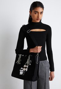 Borsa a spalla nera in canvas con una grafica che rappresenta una figura e un gatto con occhiali da sole, con dettagli decorativi in bianco e nero sulle cinghie.