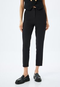 Zwarte tapering broek gemaakt van gladde stof met een middelhoge taille en zijzakken, gecombineerd met zwarte instappers.