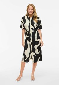 Knapplång klänning i krämfärgad och svart med abstrakt vågig mönster, korta ärmar, knytmidja och knälång skärning. Slät tygstruktur.