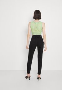 Groene gehaakte tanktop gecombineerd met zwarte high-waisted jeans. Opengehaakt ontwerp met een geometrisch patroon. Geheel wordt afgemaakt met sleehakken.