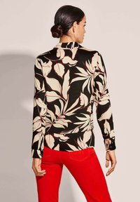 Black shirt with large floral print in cream and red, long sleeves, collar, and buttoned cuffs; paired with red pants.