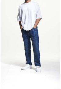 Biała oversize koszulka, niebieskie jeansy o prostych nogawkach i białe trampki. Gładka tkanina, luźny krój i minimalistyczny design. Brak widocznych wzorów lub akcentów.