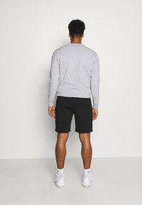 Huppari harmaalla värillä, jossa on pyöreä kaula-aukko, yhdistetty mustiin shortseihin. Mallilla on valkoiset tennarit ja nilkkasukat. Minimalistinen muotoilu, rento istuvuus.