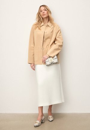 Beżowa wełniana kurtka z dużymi guzikami, biała dzianinowa spódnica midi oraz wzorzyste buty. Stylizację dopełnia teksturowana torebka z kwiatowym akcentem.