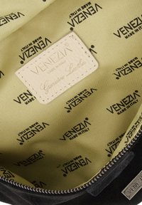 Schwarze Wildledertasche mit einem Innenfutter, das ein cremefarbenes Etikett mit der Aufschrift "VENEZIA MADE IN ITALY" und "Echtes Leder" zeigt, sowie einem gelben Stofffutter und einem sich wiederholenden Logomuster.