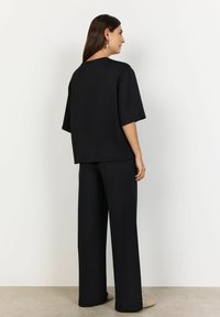 Top oversize negru, cu mâneci scurte și pantaloni largi, confecționat dintr-un material moale, având o textură fină și un design minimalist.