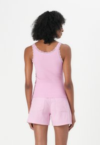 Débardeur rose à côtes avec bord en dentelle, associé à un short rayé rose et blanc. Tissu léger, coupe décontractée et détails de couture visibles.