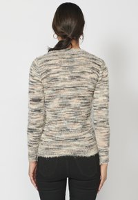 Stickad tröja i nyanser av kräm, beige och grått med ett mönster av texturerade ränder. Har långa ärmar och en rundad urringning.