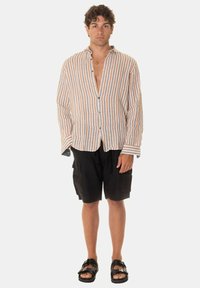 Camicia in lino a righe arancione e blu, design con bottoni, maniche larghe; abbinata a pantaloni cargo neri e sandali neri.