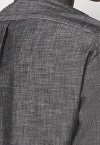 Camisa de lino gris exhibida desde la parte posterior, con un ajuste relajado, una textura sutil y un diseño de cuello simple.